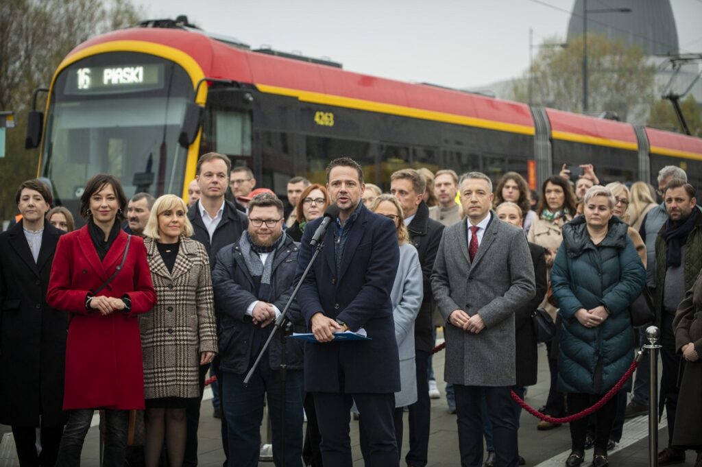 Prezydent Rafał Trzaskowski przemawia na tle ludzi i tramwaju Hyundai