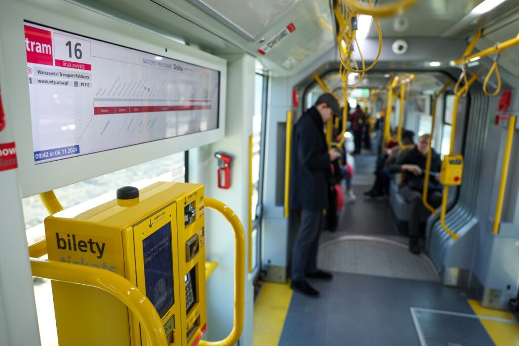 Wnętrze tramwaju linii 16, na pierwszym planie elektroniczna tablica z przebiegiem trasy oraz biletomat